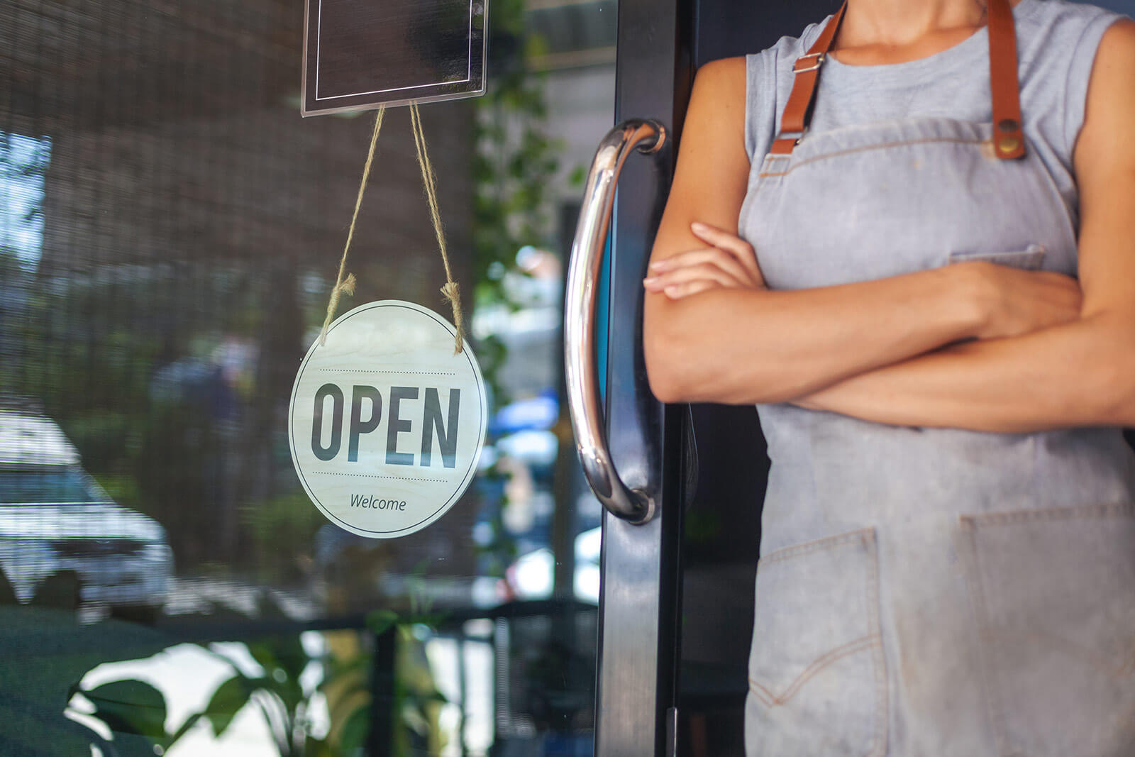 Open for Business sign next to a business owner standing at the door.