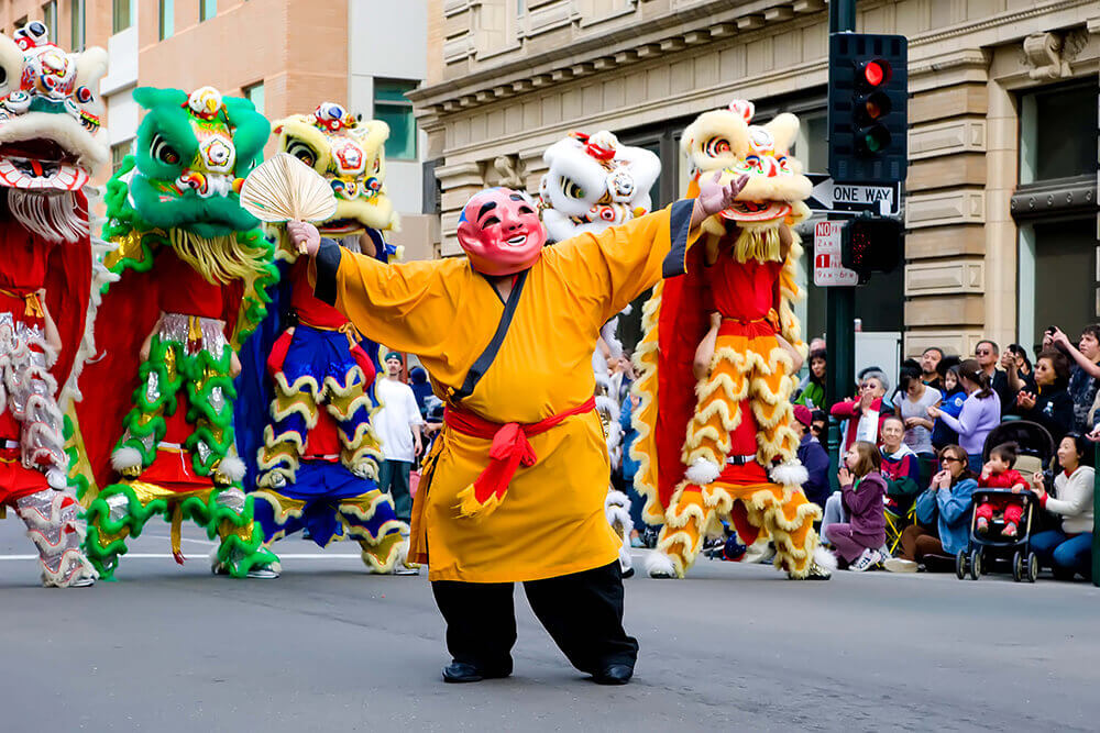 Man in costume flanked by persons in dragon costumes in a street parade